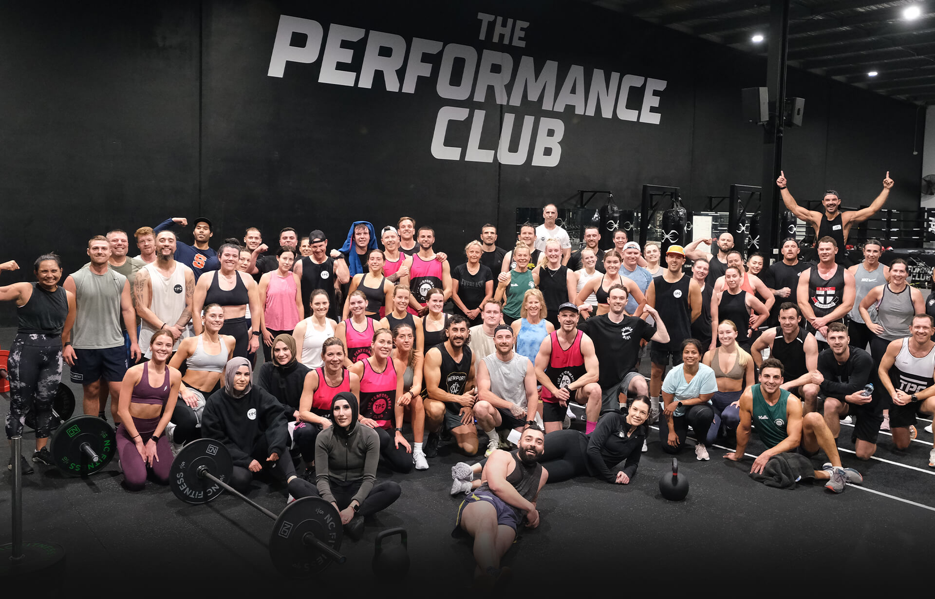 The Performance Club community packed under the gym wall, arms up and smiling
